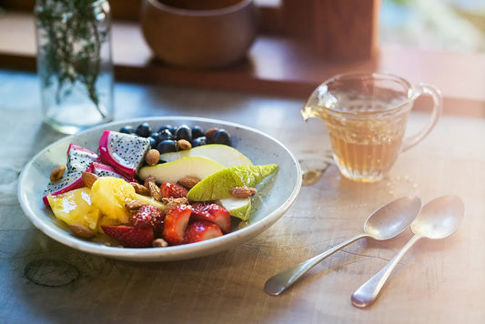 plate of fruit with honey and cutlery on table